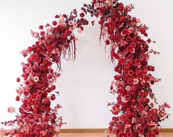 May include: A wedding arch decorated with cascading red and pink roses, creating a romantic and elegant backdrop for a ceremony.