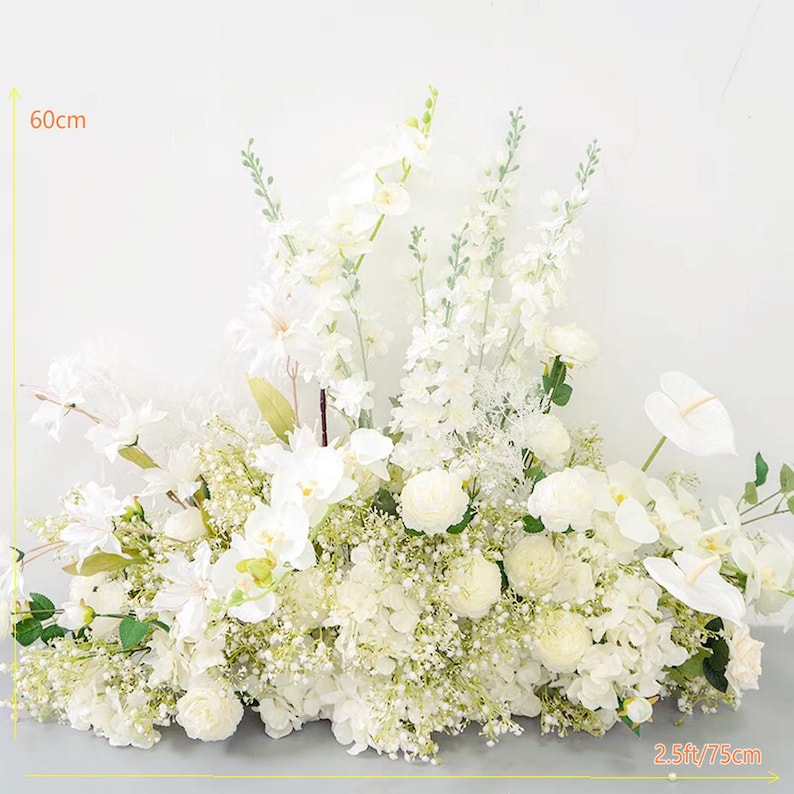 May include: A white floral arrangement with a variety of flowers, including orchids, hydrangeas, and baby's breath. The arrangement is 60 cm tall and 75 cm wide.