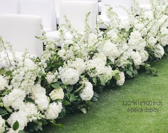 Op de afbeelding: Een bloemstuk van witte bloemen, waaronder hortensia's, met groene bladeren, gerangschikt op een groene ondergrond. Witte stoelen op de achtergrond. De tekst op de afbeelding luidt: L20*W16*H20 inch, 6 peice display. (ongeveer 51x41x51 cm).