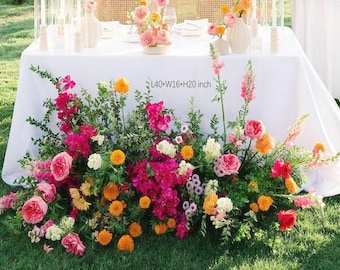 May include: A white tablecloth is adorned with a vibrant floral arrangement. The arrangement features pink, orange, and white flowers, with dimensions of L40*W16*H20 inches. The flowers are arranged on a green lawn, creating a colorful display.