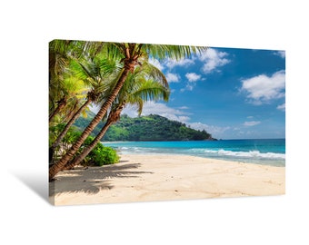 May include: A tropical beach scene with palm trees leaning over white sand and turquoise water. Lush green hills are visible in the background under a bright blue sky with fluffy white clouds.