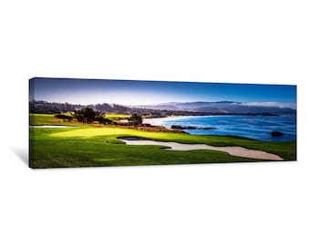 Puede incluir: Una vista panorámica de un campo de golf con un fairway verde y un bunker de arena. El campo está situado en un acantilado con vistas a un océano azul con una playa de arena en la distancia. El cielo es de un azul vibrante con nubes blancas.