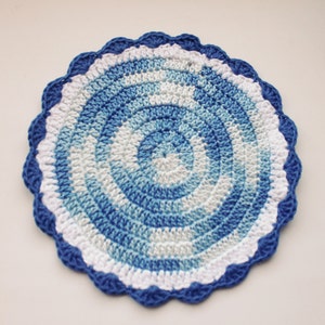 Pode incluir: Um descanso de copo de crochê azul e branco com uma borda festonada. O descanso de copo tem um padrão em espiral em tons de azul e branco.