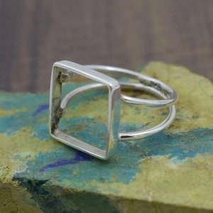 May include: A silver ring with a square frame. The ring is open on one side and has a smooth, polished finish.