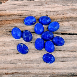 May include: A collection of oval-shaped, polished lapis lazuli gemstones in various sizes, displayed on a rustic wooden surface.