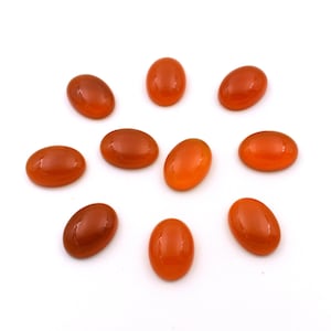 Op de afbeelding: Tien ovale carneol edelstenen in verschillende tinten oranje en rood. De stenen zijn glad en gepolijst, met een glanzende afwerking.