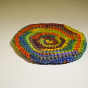 May include: A colorful crocheted coaster with a spiral pattern in shades of green, orange, brown, yellow, and blue.
