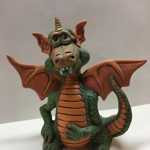 May include: A green and orange ceramic dragon figurine with a gold horn, sitting with its wings spread out.
