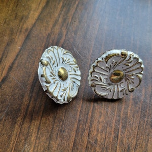 May include: Two white and gold decorative knobs with a floral design. The knobs are round and have a raised center.