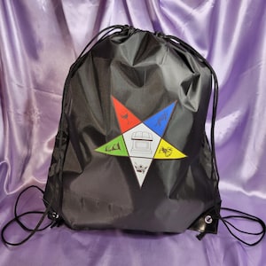 May include: Black drawstring bag with a five-pointed star design. The star has five different colored points, each with a symbol in the center. The symbols are a wine glass, a trowel, a compass, a square, and a crown.