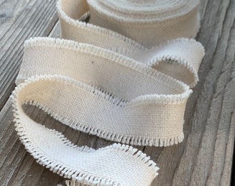 May include: A white cotton ribbon with a frayed edge. The ribbon is rolled up and lying on a wooden surface.