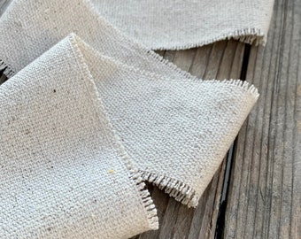 May include: A roll of natural linen ribbon with a frayed edge. The ribbon is folded and displayed on a wooden surface.