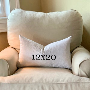 May include: A white pillow with the text "12x20" printed on it. The pillow is sitting on a beige armchair.