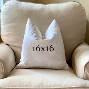 May include: A white pillow with the text "16x16" printed on it, sitting on a beige armchair.