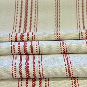 Puede incluir: Tela de color crema con rayas rojas. Las rayas están hechas de pequeños puntos rojos. La tela está doblada en tres.