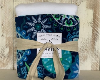 May include: A blue and green patterned fleece blanket is rolled up and tied with a tan ribbon. The ribbon has a tag that says "Sunny Slope Farms" and "Hug it on the Sunny Side".