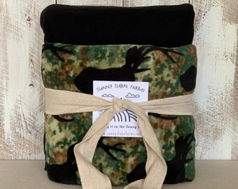 May include: A set of two fleece blankets, one black and one camouflage with a deer silhouette, tied together with a beige ribbon. The label reads "Sunny Slope Farms" and includes a website address.