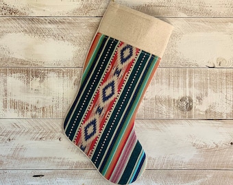Könnte beinhalten: Ein bunter Weihnachtssocken mit einem geometrischen Muster in Rot-, Orange-, Blau-, Grün- und Weißtönen. Der Socken hat einen braunen Bund.