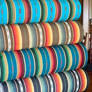 May include: Four rolls of colorful striped fabric stacked on top of each other. The fabric has a southwestern pattern with stripes of turquoise, orange, brown, red, and yellow.