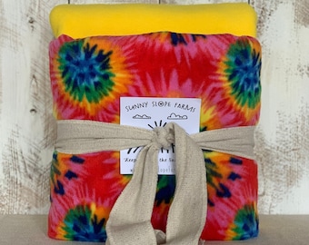 May include: A red, blue, and yellow tie-dye fleece blanket is wrapped in natural twine and tied with a bow. The blanket is packaged with a yellow fleece blanket. A tag with the text "Sunny Slope Farms" is attached to the twine.