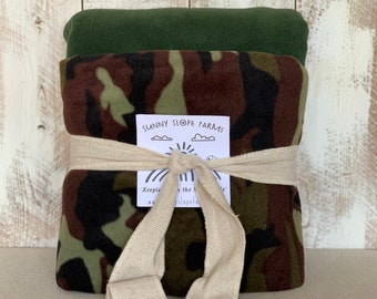 May include: A camouflage fleece blanket is wrapped in a beige ribbon with a white tag that reads "Sunny Slope Farms" and "Keeping it the simple way".