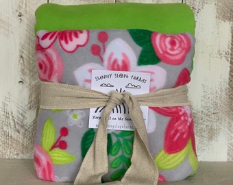 May include: A gray and white fleece blanket with a floral pattern in pink, green, and white. The blanket is tied with a tan ribbon and has a tag that says "Sunny Slope Farms" and "Keep it on the sunny side".