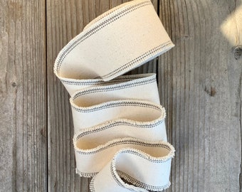 May include: A roll of off-white cotton ribbon with black stitching. The ribbon is folded and has a frayed edge.