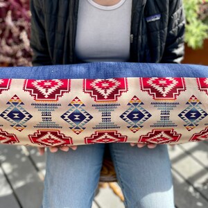 May include: A long, rectangular pillow with a denim border and a cream-colored fabric with a geometric pattern in shades of red, blue, and yellow.