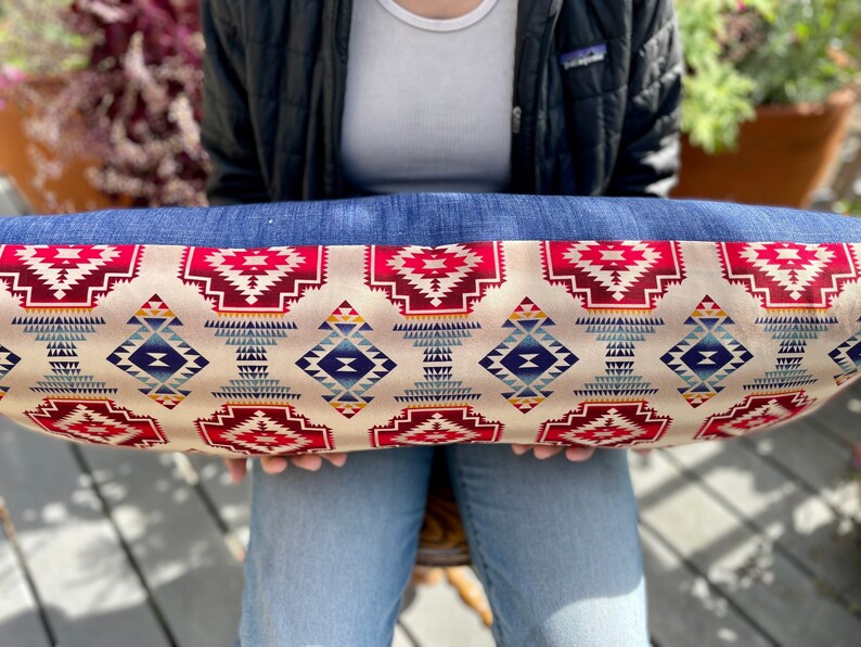 May include: A long, rectangular pillow with a denim border and a cream-colored fabric with a geometric pattern in shades of red, blue, and yellow.