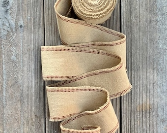 May include: A roll of beige burlap ribbon with red stitching. The ribbon is rolled up and has a frayed edge.