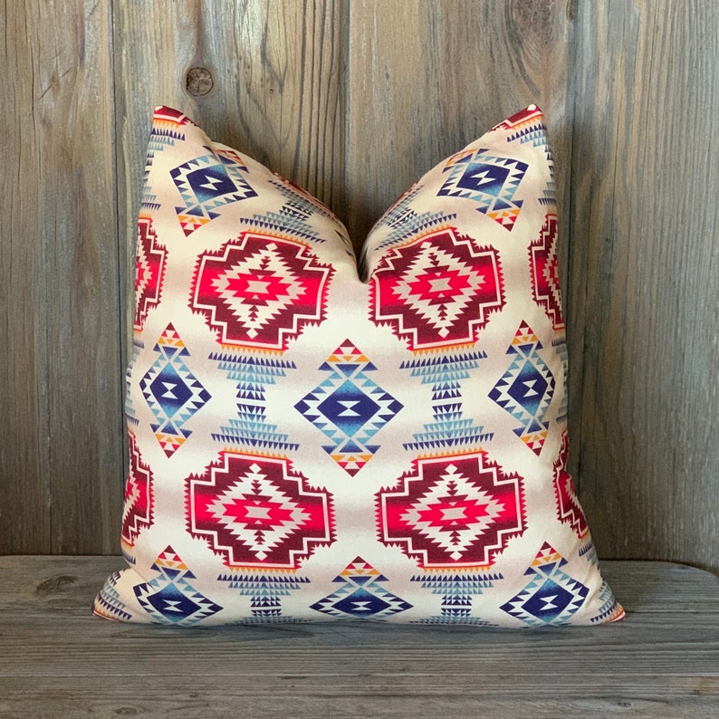 May include: A decorative throw pillow with a geometric pattern in shades of red, blue, and yellow on a cream background.