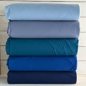 May include: A stack of six rolled fabric pieces in varying shades of blue. The colors range from light sky blue to deep navy. The fabric appears soft and possibly fleece or flannel.