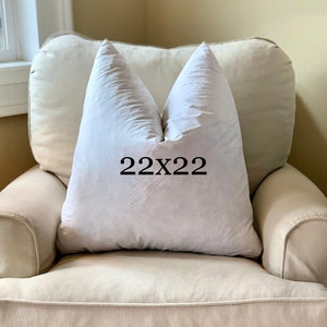 May include: A white pillow with the text "22x22" printed on it, sitting on a beige armchair.