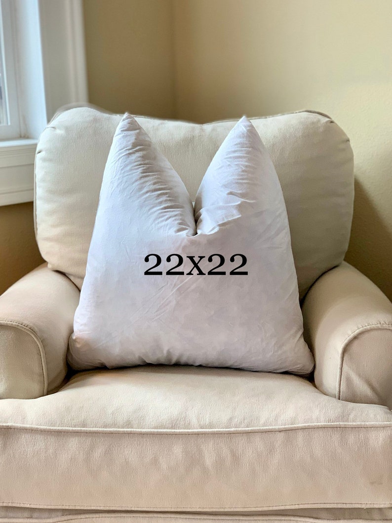May include: A white pillow with the text "22x22" printed on it, sitting on a beige armchair.