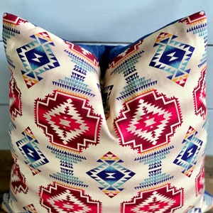 May include: A decorative pillow with a geometric pattern in shades of red, blue, and yellow on a cream background. The pillow has a denim-like fabric backing.