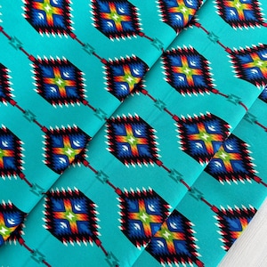 Puede incluir: Tela turquesa con un patrón repetido de diamantes geométricos coloridos. Los diamantes tienen un contorno negro y están llenos de una variedad de colores, incluyendo rojo, naranja, amarillo, verde, azul y blanco.