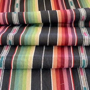 May include: Folded fabric with a striped pattern. The design features vertical stripes in a spectrum of colours, including red, orange, green, and purple, set against a black background with white lines.