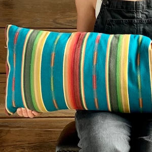 May include: A teal, yellow, red, and green striped throw pillow. The pillow is made of a soft, woven fabric.