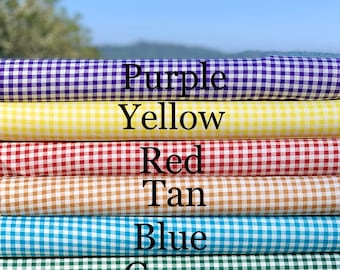 Könnte beinhalten: Ein Stapel aus sechs Gingham-Stoffmustern in verschiedenen Farben: Lila, Gelb, Rot, Braun, Blau und Grün. Der Stoff ist gefaltet und auf einer Holzoberfläche gestapelt.