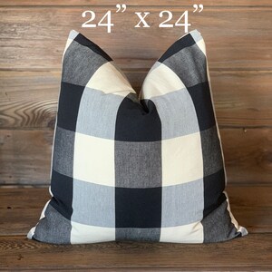May include: A square pillow with a black, white, and gray buffalo check pattern. The pillow measures 24 inches by 24 inches. The pillow is a decorative item for a bed or sofa.