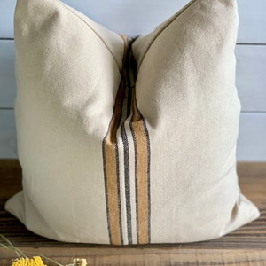 May include: A beige pillow with a brown, black, and white striped design down the center.