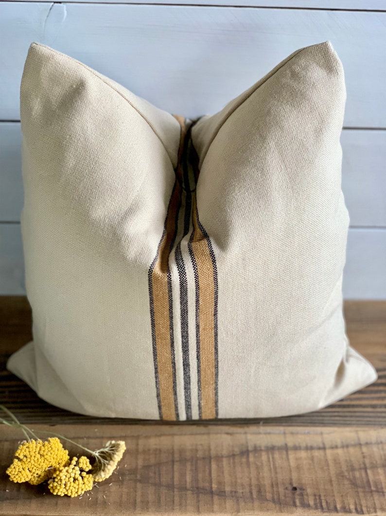 May include: A beige pillow with a brown, black, and white striped design down the center.