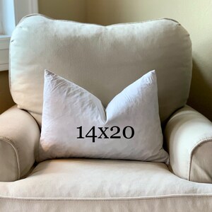 May include: A white pillow with the text "14x20" printed on it, sitting on a beige armchair.