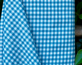 Puede incluir: Una tela de cuadros vichy azul y blanca con un pequeño patrón de cuadros. La tela está doblada por la mitad y los bordes son visibles.