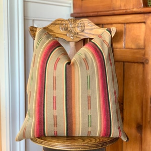 May include: A decorative pillow with a striped pattern in shades of tan, red, brown, and green. The pillow is placed on a wooden chair with a carved back. The pillow's design features vertical stripes.