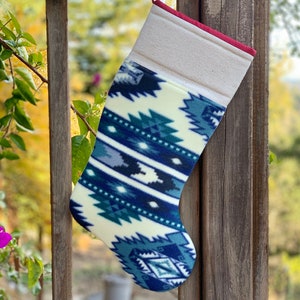 May include: A white and blue patterned Christmas stocking with a red cuff. The stocking is hanging on a wooden railing.