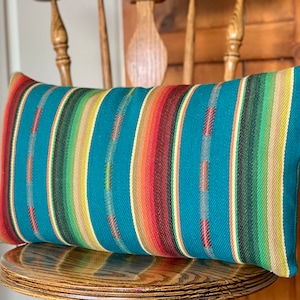 May include: A teal blue, green, yellow, red, and brown striped throw pillow. The pillow is sitting on a wooden chair.
