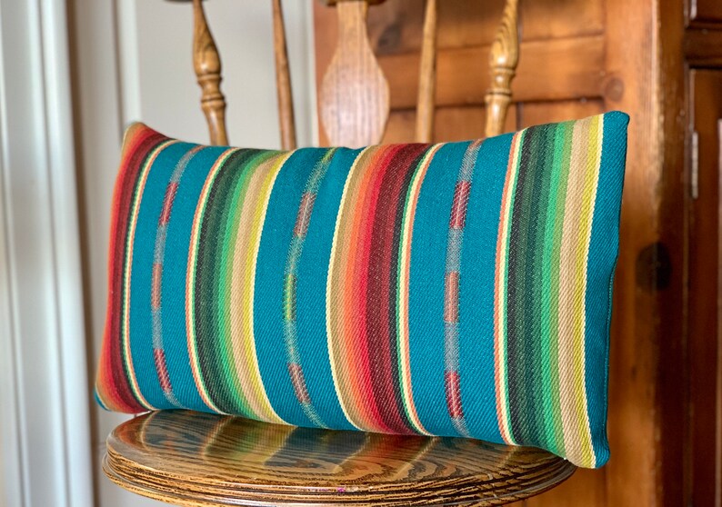 May include: A teal blue, green, yellow, red, and brown striped throw pillow. The pillow is sitting on a wooden chair.