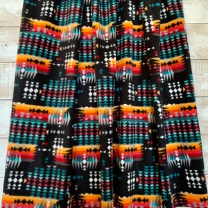 May include: Black fleece fabric with a colorful geometric pattern. The pattern features a variety of shapes, including triangles, squares, and diamonds. The colors in the pattern include red, orange, yellow, green, blue, and white.