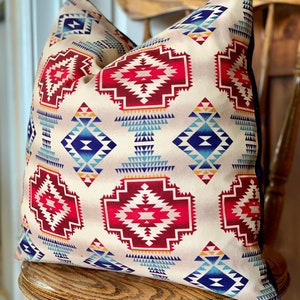 May include: A beige throw pillow with a geometric pattern in shades of red, blue, and yellow. The pattern is reminiscent of Native American designs.
